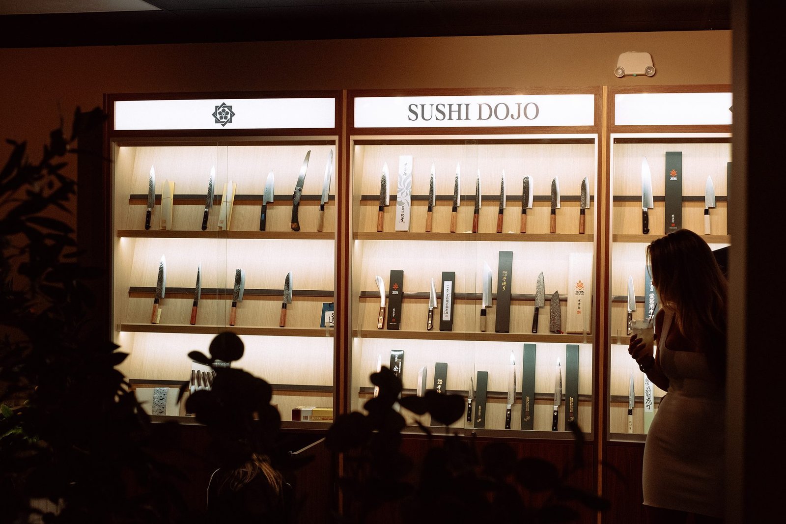 The knife case at Sushi Dojo — rows of Japanese blades lit behind glass beneath the restaurant's wordmark.