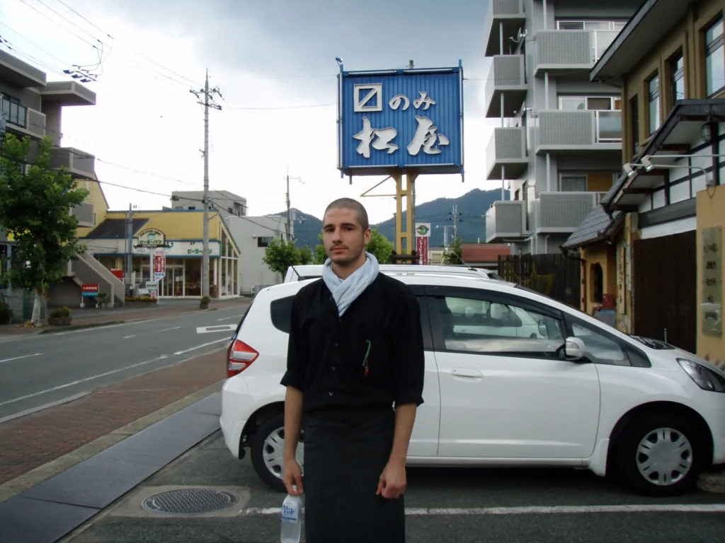 Chef David on a street in Japan, outside a shop with a blue noren
