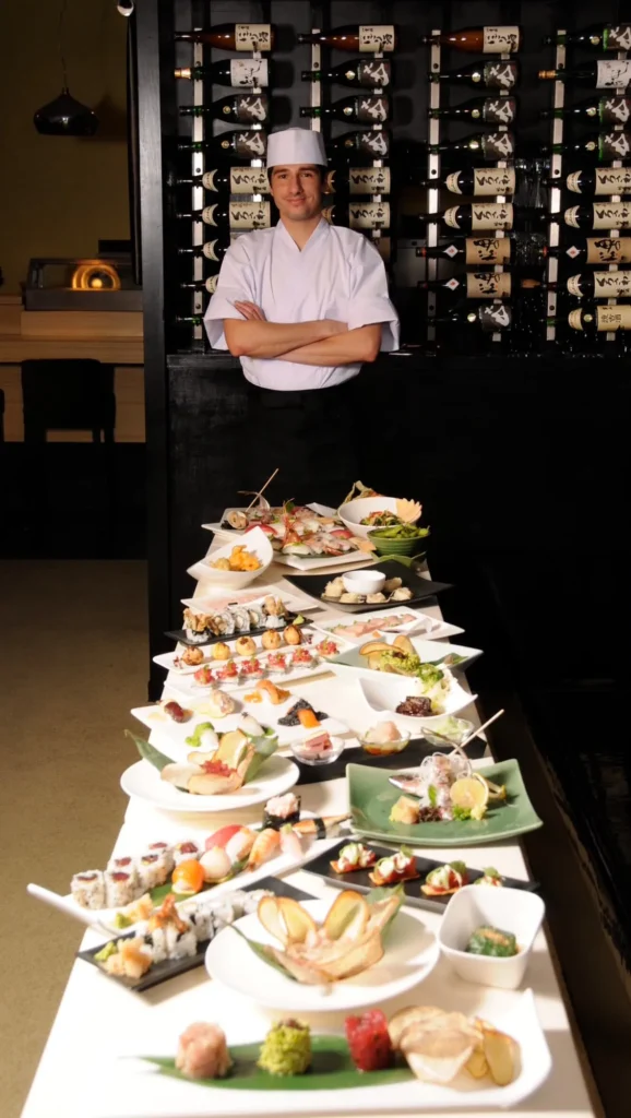 Platters of sushi plated for an event, the chef in his white coat behind the table